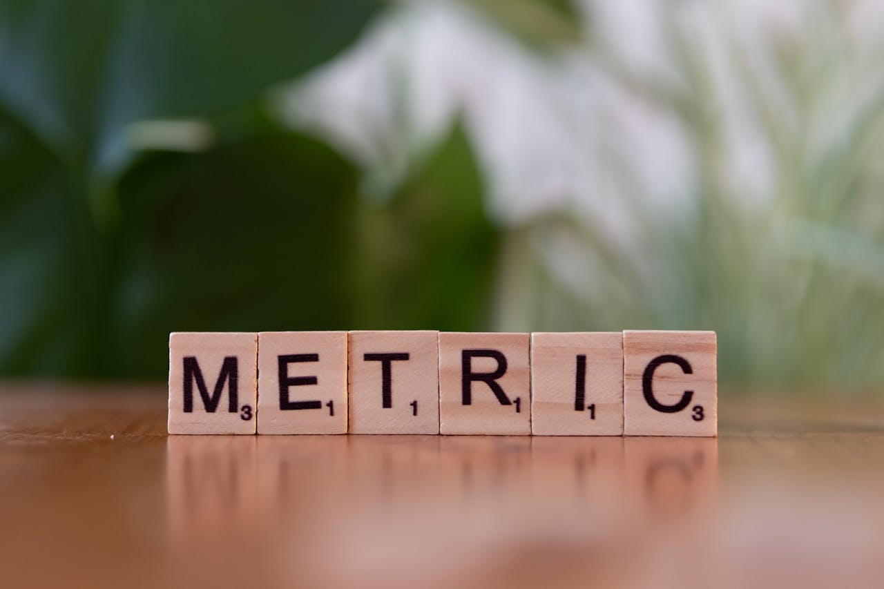 Close-up of wooden tiles spelling 'Metric' on a table, with a blurred green background.